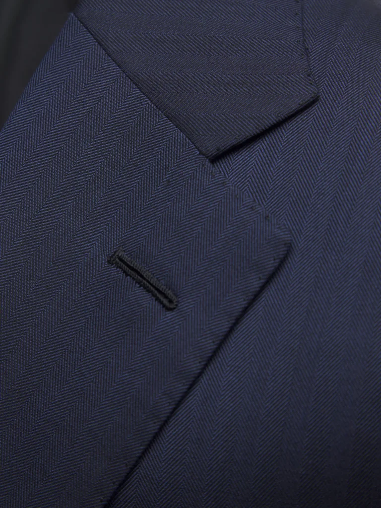 Close-up of hand-stitched detail on a tailored navy blue blazer lapel, conveying quiet luxury craftsmanship